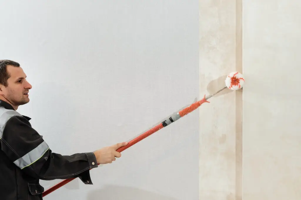 Man worker applies glue with a paint roller on the walls before wallpapering or primer on the walls, selective focus. Apartment renovation and restoration idea indoors.